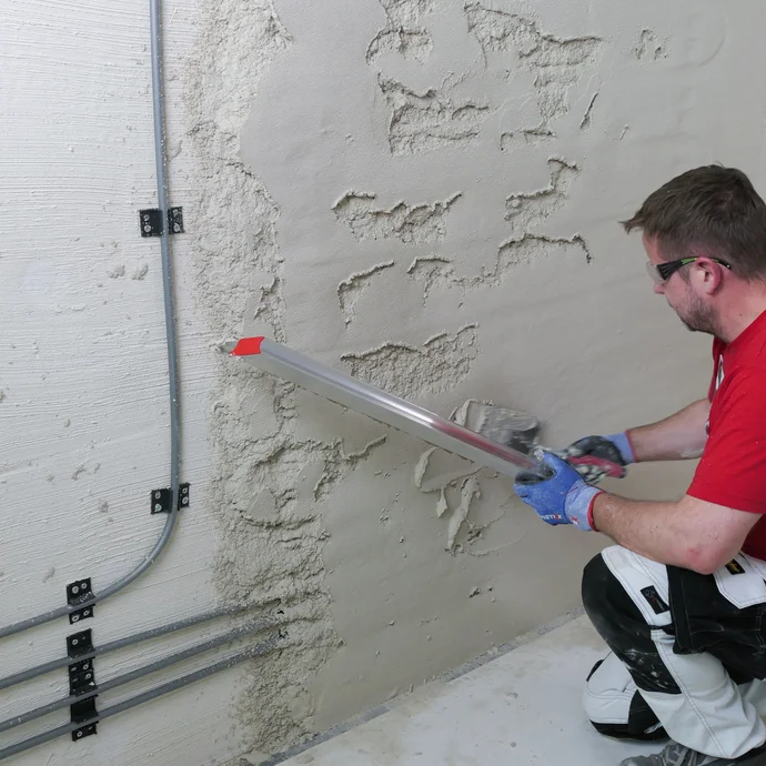Mann bessert ungleichm&auml;&szlig;ig verputzte Stellen an der Wand mit Putzmaterial und Abziehlatte aus.