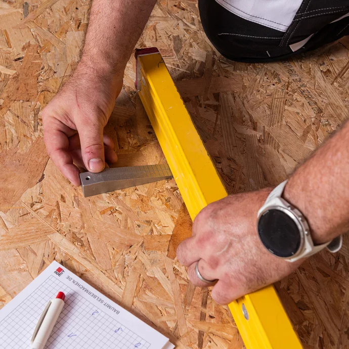Detailfoto: Mit einem Messkeil und einer Wasserwaage werden die Unebenheiten des Holzbodens ermittelt. Die Werte werden mit Kulli auf einem Blick notiert.