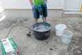 Handyman mengt Munich roughcast met water en een elektrische mixer in een mortelemmer.