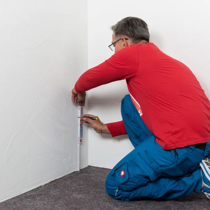 Handwerker misst die Einbauh&ouml;he zur Anbringung der Horizontalabdichtung aus und markiert die Position mit einem Bleistift an der Wand.