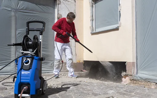 Heimwerker reinigt die Fassade mit einem Hochdruckreiniger und klarem Wasser, nachdem hohlliegende Stellen an der Fassade abgeschlagen wurden. Jetzt kann die Fassadensanierung beginnen.