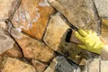 Hand reinigt eine Natursteinfassade mit einer Bürste und Seifenwasser.