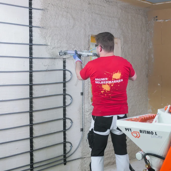 Heimwerker tr&auml;gt mit einer Putzmaschine mineralischen Putz auf eine Wand mit Wandheizung auf.