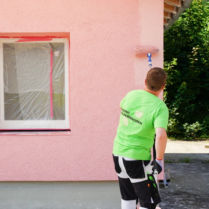 Mann trägt zweite Lage Fassadenanstrich an der Wand auf.