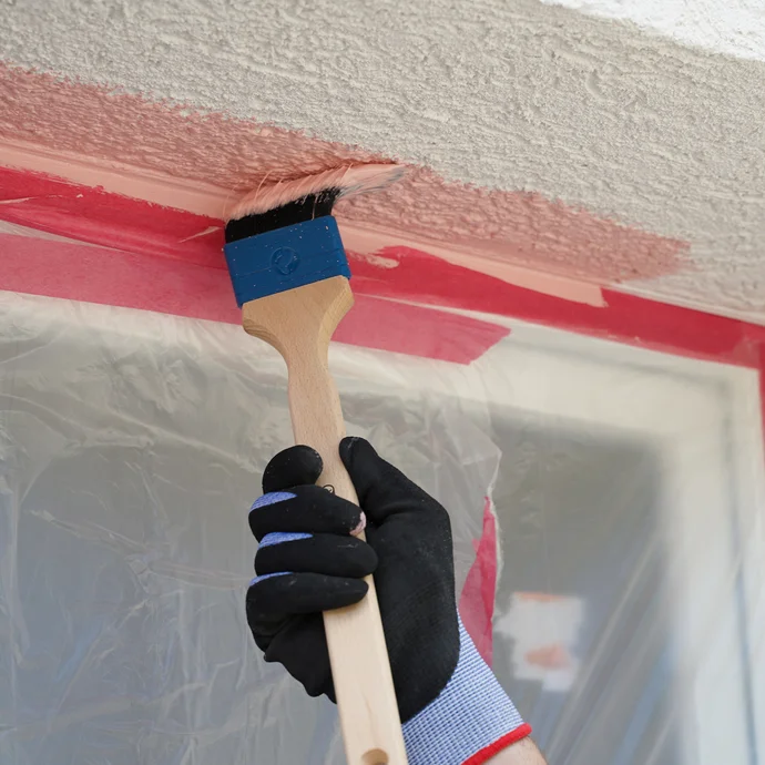 Person streicht Laibung eines Fensters mit einem Pinsel an.