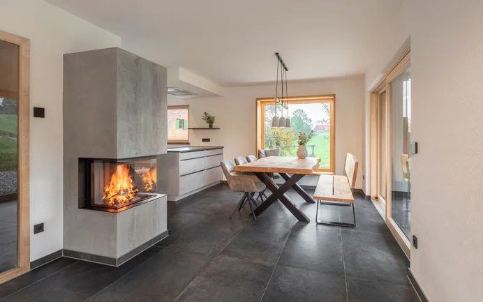 Modern ingerichte woonkamer met een haard in betonlook, een granieten vloer, moderne meubels en de fijne, stralend witte structuurpleister InStyle Edelwit voor een gezond woonklimaat.