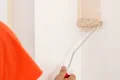 Heimwerker streicht Innenwand mit Rolle in Beige, Schritt-für-Schritt-Anleitung für Malerarbeiten.