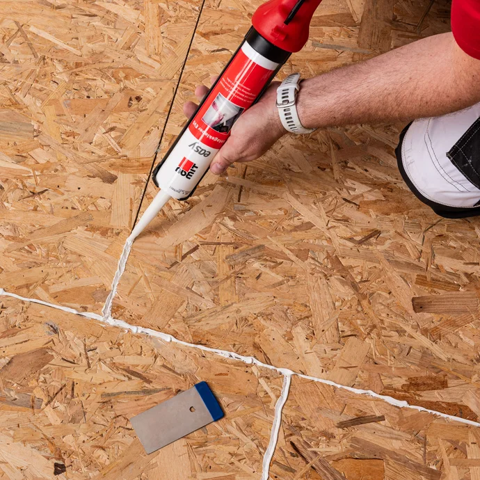 Detailfoto: die Stoßfugen der Spanplatten am Boden werden mit dem easy Montagekleber EVO von Baumit abgedicht.