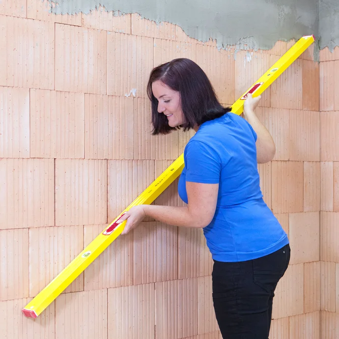 Frau prüft die Wand auf Unebenheiten mit einer langen Wasserwaage.