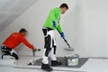 De airless en roller plamuur silicaat wordt aangebracht door één persoon met een roller en de andere persoon strijkt de plamuur glad.