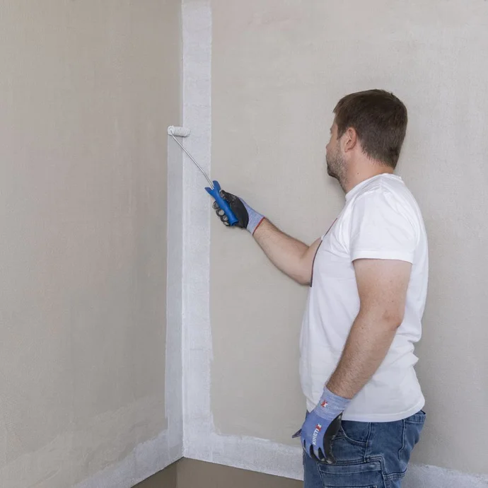 Person tr&auml;gt Grundierung an der Innenecke einer Wand mit einer kleinen Farbrolle auf.