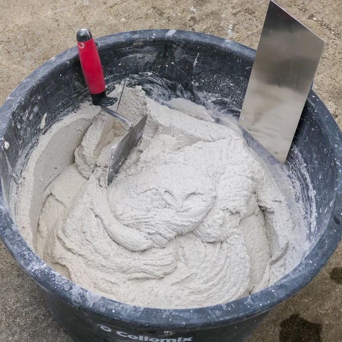 Mörtelkübel mit frisch angemischten Rauputz- im Mörtelkübel ist eine Glättkelle und Maurerkelle zu sehen.