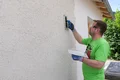 Heimwerker textureert de Munich roughcast met een plastic wrijfplank in cirkelvormige bewegingen.