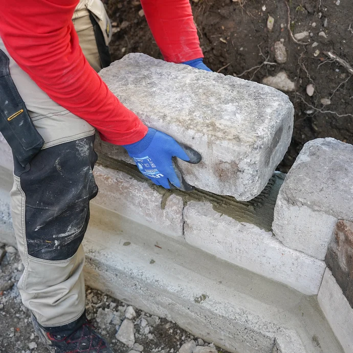 Person platziert einen schweren Mauerstein in den zuvor aufgetragenen und aufgezahnten Steinkleber.