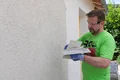 Handyman structureert de Munich roughcast en schraapt het bindmiddel eraf met de troffel.