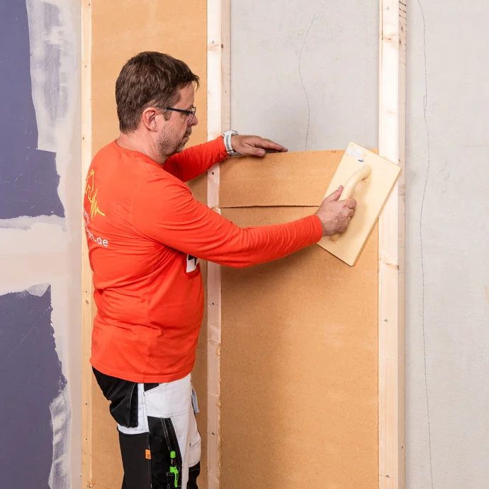 Handwerker setzt ein Teilstück der Holzfaserdämmplatte in den Zwischenraum der Tragkonstruktion ein. Anleitung Baumit Selbermachen.