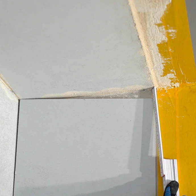 Mit einem Meterstab wird das Ma&szlig; ermittelt, sodass der Anschlusskeil an der Wand b&uuml;ndig zur Decke zugeschnitten werden kann.