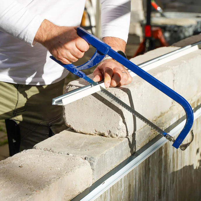 Handwerker sägt mit einer blauen Eisensäge ein Abschlussprofil auf der Mauer auf die richtige Länge zu.