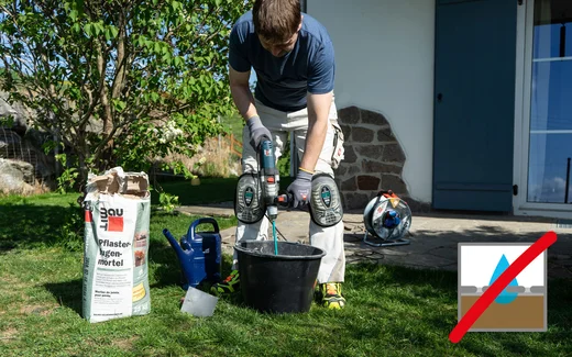 Person r&uuml;hrt mit einem elektrischen R&uuml;hrger&auml;t den Pflasterfugenm&ouml;rtel im Garten an.