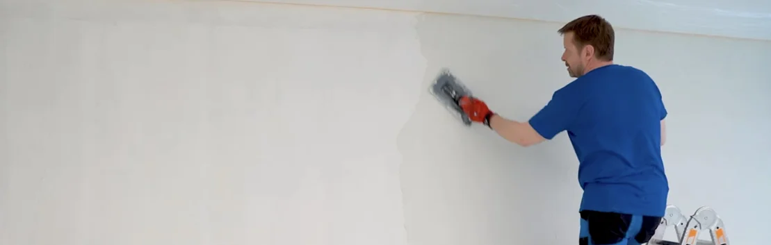 Heimwerker tr&auml;gt mit einer Kelle Putz auf eine Innenwand auf, um sie f&uuml;r das Streichen vorzubereiten.