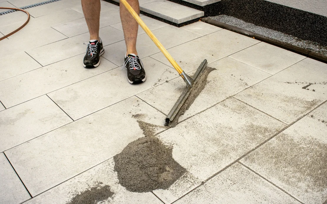 Der Pflasterfugenm&ouml;rtel Fix von Baumit wird mit einem Gummischieber in die Fugen der Terrassenplatten verteilt.