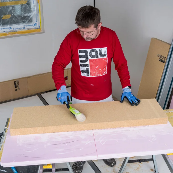 Heimwerker kehrt die Klebeseite einer Holzfaserd&auml;mmplatte mit einem Pinsel gr&uuml;ndlich ab &ndash; Staub und Schmutz entfernen f&uuml;r eine optimale Haftung des Baumit Klebem&ouml;rtels, Baumit Selbermachen Anleitung.