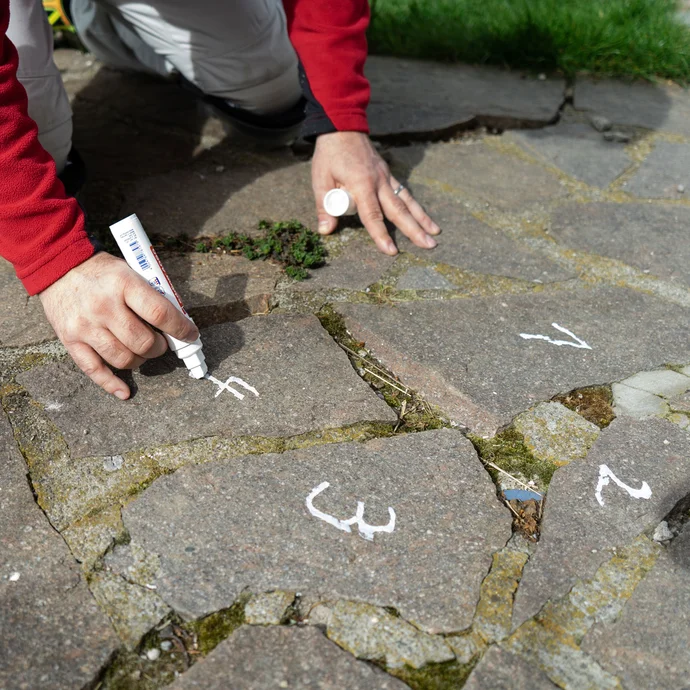 Person markiert lose Natursteinplatten mit einem weißen Kreidestift zur späteren Wiederverlegung.“