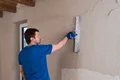 Mann glättet Innenwand mit Spachtelwerkzeug, Heimwerkeranleitung zur Wandrenovierung von Baumit.