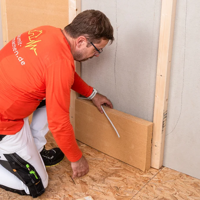 Heimwerker verlegt in der ersten Dämmebene mit Holzfaserdämmplatten auf Tragkonstruktion die Elektroleitung bzw. das Leerrohr für die Kabel. Anleitung zum Selbermachen mit Baumit.