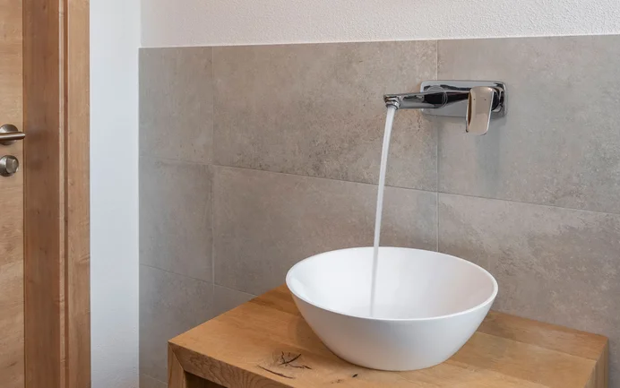 Moderne, witte wastafel met stromend water op een houten dressoir, gecombineerd met stijlvolle grijze wandpanelen en afwerkpleister met een gevilte structuur voor een gezond woonklimaat.