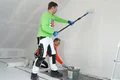 De airless en roller plamuur silicaat wordt aangebracht door één persoon met een roller en de andere persoon strijkt de plamuur glad.