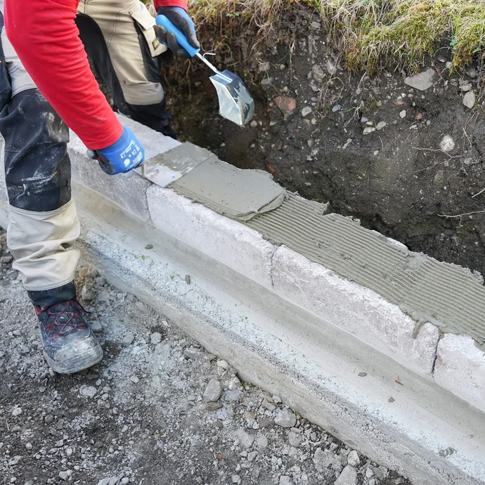Steinkleber wird mit einer Glättekelle gleichmäßig auf eine Mauer aus Betonsteinen aufgetragen.