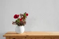 Vase mit roten Blumen auf Holzregal vor weiß verputzter Wand, ideale Inspiration für Innenraumdekor mit Baumit-Produkten.