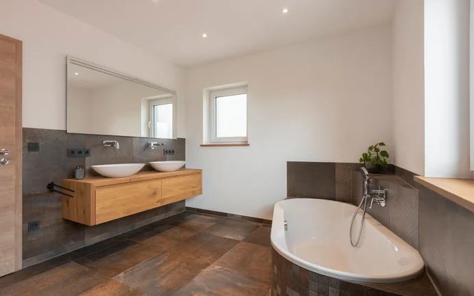Modern ontworpen badkamer met verschillende donkere, roestkleurige platen die perfect tot hun recht komen dankzij de stralend witte muren met een fijne, gevilte structuur, gemaakt met de Baumit-afwerkpleister InStyle Edelwit.