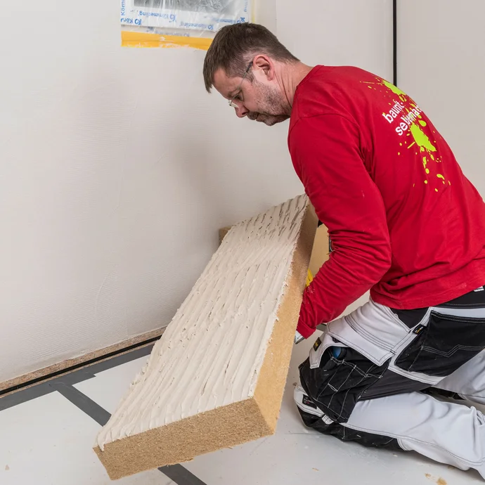Heimwerker klebt mit Baumit Klebem&ouml;rtel vollfl&auml;chig beschichtete Holzfaserd&auml;mmplatte kr&auml;ftig an die Innenwand &ndash; D&auml;mmplatte fest andr&uuml;cken f&uuml;r eine vollfl&auml;chige und w&auml;rmebr&uuml;ckenfreie Verklebung der Innend&auml;mmung, Baumit Selbermachen Anleitung.
