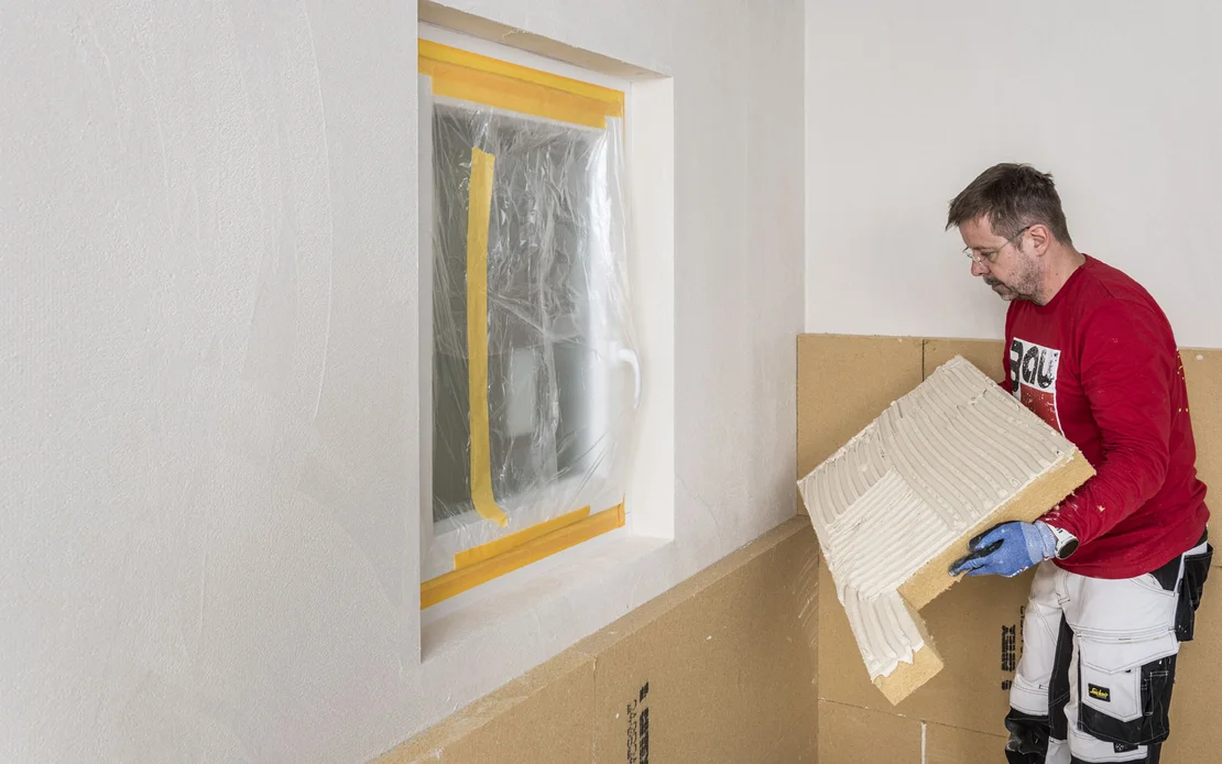Heimwerker klebt Holzfaserd&auml;mmplatte an die Wand. Die D&auml;mmplatte ist in L-Form zugeschnitten. Baumit Selbermachen DIY-Anleitung.