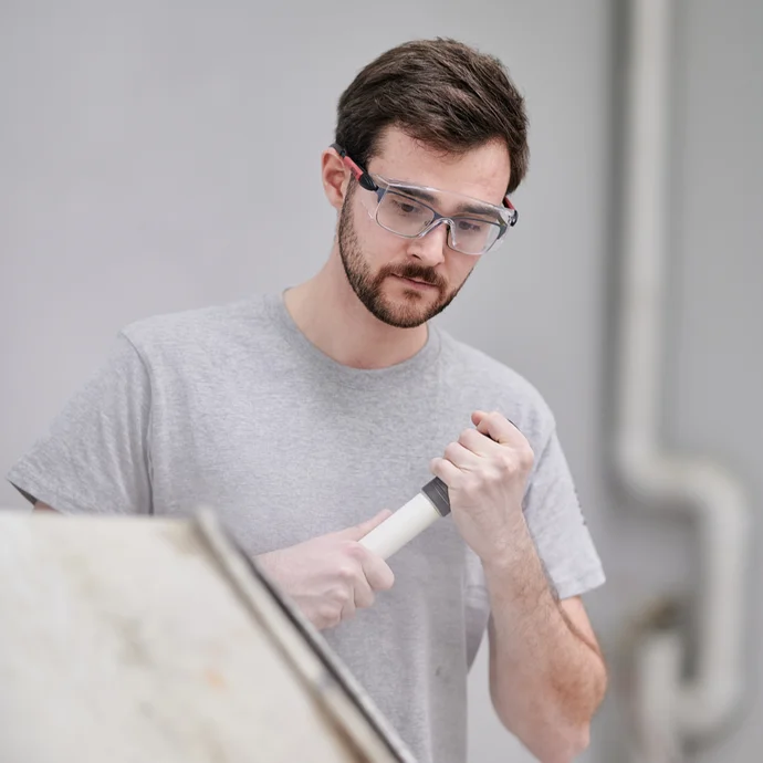 Mann verwendet Spachtelmasse mit Werkzeug, tr&auml;gt Schutzbrille, ideal f&uuml;r Heimwerker bei Renovierungsarbeiten.