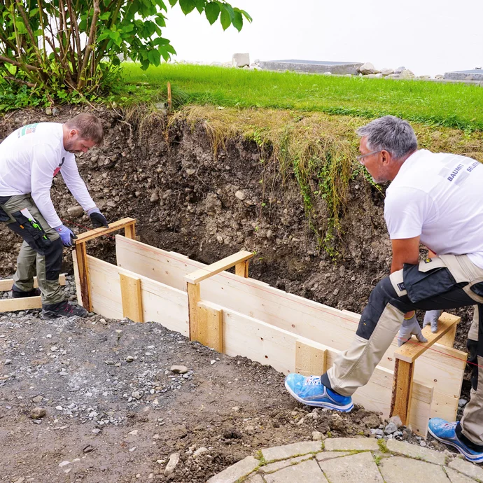 Die fertig montierten Schalungselemente werden zu zweit in die Baugrube gesetzt.