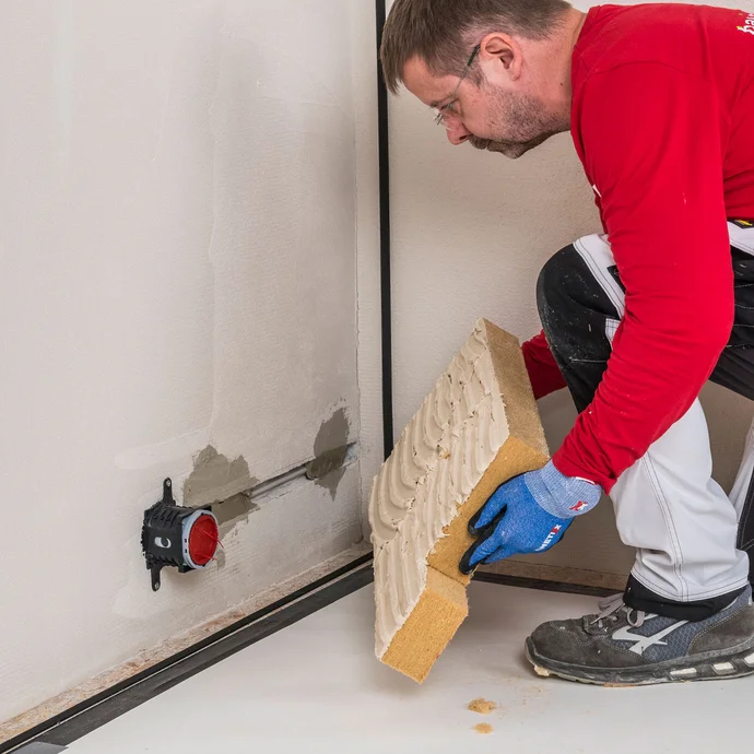 Heimwerker setzt mit Baumit Klebem&ouml;rtel beschichtete Holzfaserd&auml;mmplatte passgenau an der Innend&auml;mmungsdose an &ndash; D&auml;mmplatte mit Steckdosenaussparung sauber und vollfl&auml;chig an die Wand kleben, Baumit Selbermachen Anleitung.